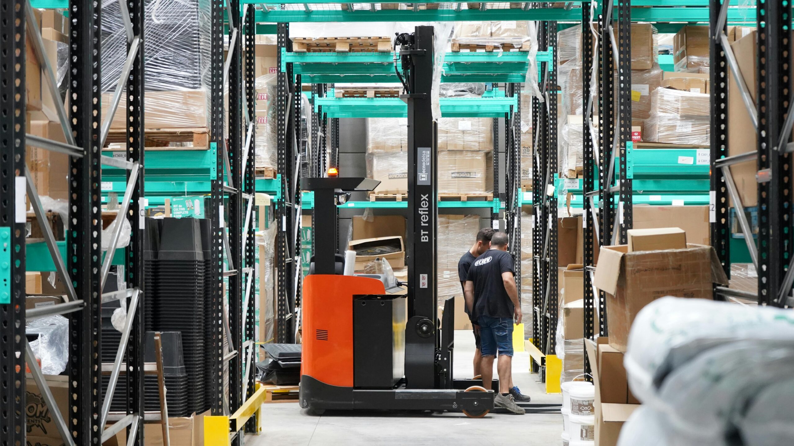 Warehouse scene featuring workers and a forklift navigating aisles for logistics and inventory management.